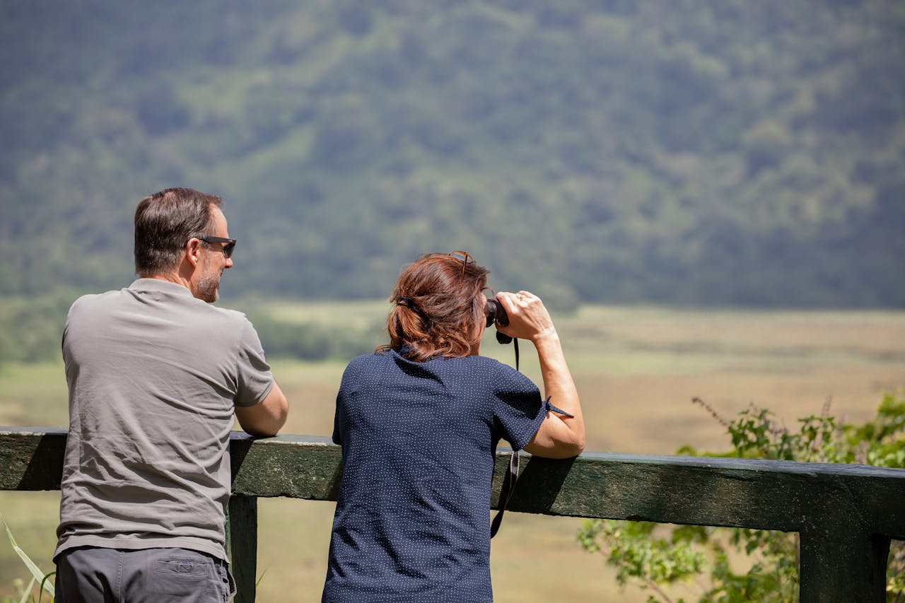 A couple relaxing outdoors, using binoculars to enjoy a scenic landscape view.