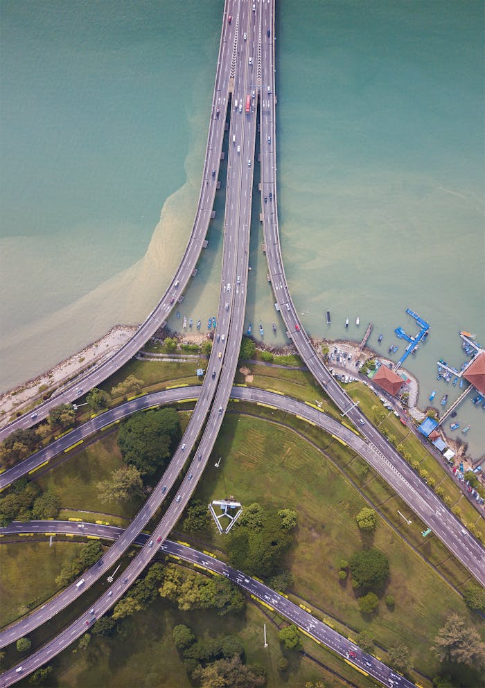 Aerial shot capturing an intricate highway and bridge network above a vibrant waterway, surrounded by green spaces.
